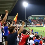 Exciting outdoor kooralive football match scene with cheering fans and players.