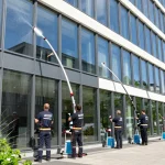 Professionelle Glasreinigung in Dortmund mit Reinigungsteam, das Fenster und Rahmen säubert, unter strahlendem Sonnenschein, umweltfreundliche Reinigungsmittel verwendet.